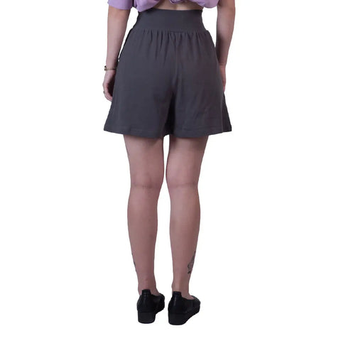 A person stands facing away from the camera wearing Spiritex | Sustainable Apparels Lexi Lounge Shorts in dark gray, a lavender top, black shoes, and bracelets, with tattoos visible on their calves against a white background.