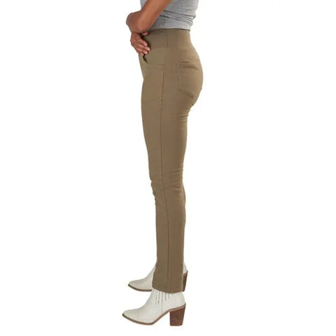 A person wearing Spiritex Lightweight Saratoga Pants stands sideways in fitted high-waisted tan pants, a grey top, and white heeled ankle boots, with one arm bent and hand resting near their chin.