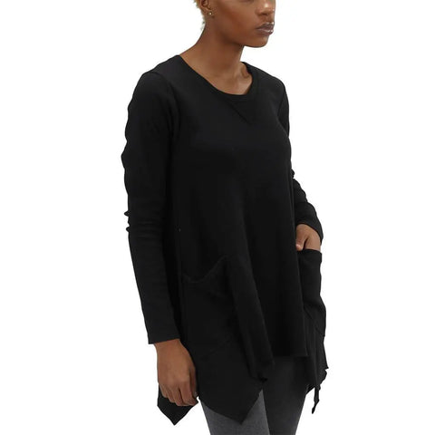 A person wearing the Spiritex | Sustainable Apparel Long Sleeve Jenna Hippie Top with two large front pockets and gray leggings, standing against a white background.
