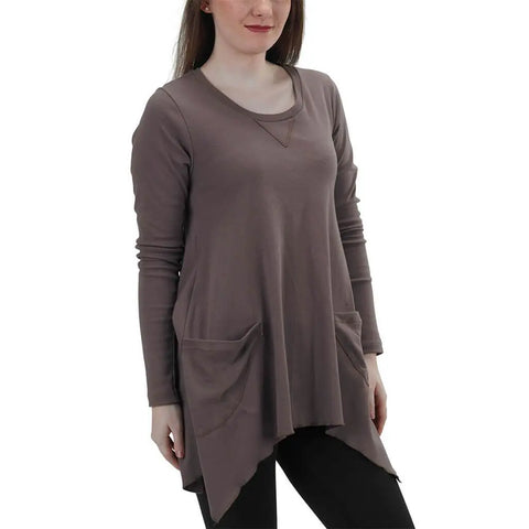 A woman in a Long Sleeve Jenna Hippie Top by Spiritex | Sustainable Apparel—mauve, loose-fitting with two front pockets and an asymmetrical hem—paired with black leggings, stands against a plain white background.