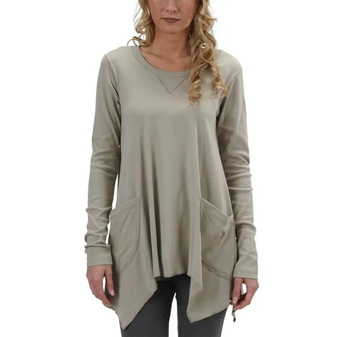 A woman wearing the Long Sleeve Jenna Hippie Top by Spiritex | Sustainable Apparel stands facing forward. The loose-fitting taupe tunic, made in the USA, features two large front pockets. She has loose curls and pairs it with dark pants.