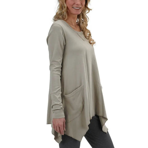 A smiling woman with wavy blonde hair wears the Spiritex Long Sleeve Jenna Hippie Top, featuring large front pockets and an asymmetrical hem, paired with dark pants. She is facing slightly to the side.