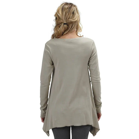 A woman with wavy blonde hair, seen from behind, wears the Spiritex | Sustainable Apparel Long Sleeve Jenna Hippie Top—an organic cotton tunic with an asymmetrical hem—over dark gray leggings.