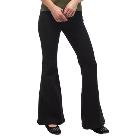 A person wearing Spiritex | Sustainable Apparel Lycra Bell Bottoms in black, paired with a green top and studded black flats, stands against a white background.