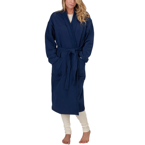 A woman with long blonde hair stands barefoot against a white background, wearing Spiritex | Sustainable Apparels Mid-Length Fleece Robe in navy blue over white pajamas. The organic cotton robe features a belt and pockets.