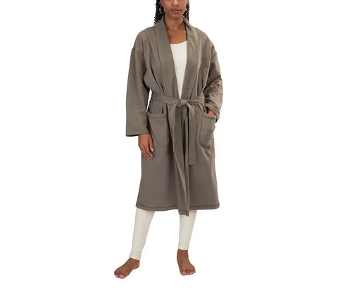 A person models the Spiritex | Sustainable Apparel Mid-Length Fleece Robe in taupe, featuring a belt and large front pockets, layered over cream loungewear and worn barefoot against a white background.