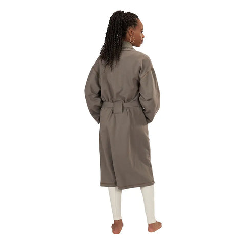 A woman with long, curly hair stands barefoot, facing away in a gray Spiritex Mid-Length Fleece Robe made from organic cotton, belted at the waist over white leggings, set against a white background.