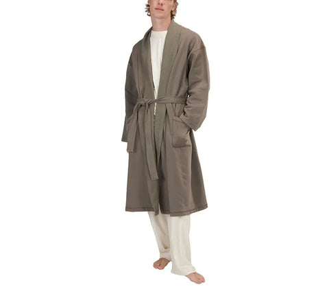 A barefoot person models cream pants, a white shirt, and the Spiritex | Sustainable Apparel Mid-Length Fleece Robe—an organic cotton, belted, unisex design—against a plain white background.