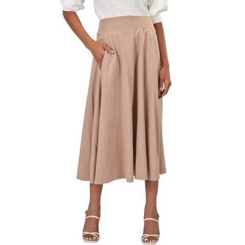 A woman models the Spiritex | Sustainable Apparel Gore Skirt—a high-waisted, light beige organic cotton A-line skirt with pockets—paired with a white blouse and white heeled sandals. Only her body from shoulders down is visible.