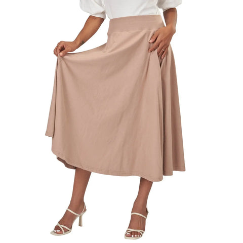 A person stands holding out the sides of the Gore Skirt by Spiritex | Sustainable Apparel, showcasing its flowy organic cotton design while wearing a white top and white high-heeled sandals.