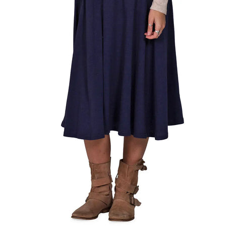 A person is shown from mid-torso down wearing the Spiritex | Sustainable Apparel Gore Skirt in navy blue, paired with tan buckle ankle boots and a beige long-sleeve top against a white background.