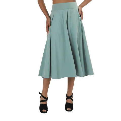 A woman wears the Spiritex Gore Skirt, a light teal, high-waisted A-line piece made from organic cotton, styled with black strappy high-heeled sandals.