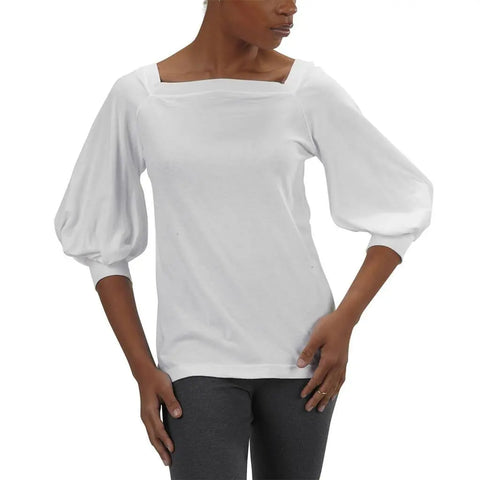 A woman wearing the Romantic Top by Spiritex | Sustainable Apparel—a white organic cotton top with a square neckline and three-quarter bishop sleeves—paired with dark gray leggings, stands with one hand on her hip.
