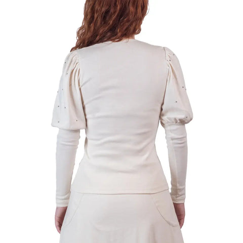A person with wavy, reddish-brown hair is shown from the back in a cream Victoria Top by Spiritex | Sustainable Apparel, made from organic cotton with puffed short sleeves over long fitted sleeves, paired with a matching skirt against a white background.