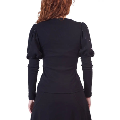 A person with wavy, reddish-brown hair is seen from behind wearing the Spiritex | Sustainable Apparel Victoria Top in fitted black organic cotton with puffed sleeves and a black skirt, accented by silver studs against a plain white background.