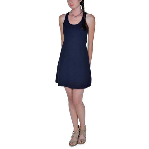 A woman models the Spiritex | Sustainable Apparel Racerback Tank Dress—sleeveless and dark navy blue—ideal for a capsule wardrobe, paired with beige sandals, standing relaxed against a white background.