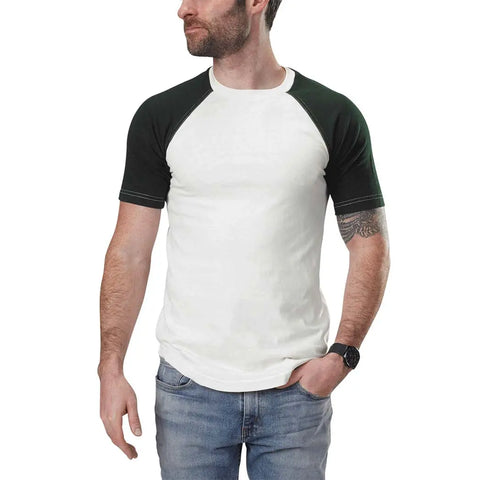 A bearded man stands with one hand in his pocket against a white background, wearing the Spiritex | Sustainable Apparel Short Sleeve Baseball Raglan Tee with black sleeves, blue jeans, and a black watch.