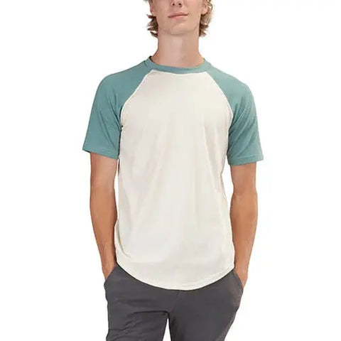 A person wearing a cream Short Sleeve Baseball Raglan Tee by Spiritex | Sustainable Apparel with green sleeves and gray pants stands with hands in pockets.
