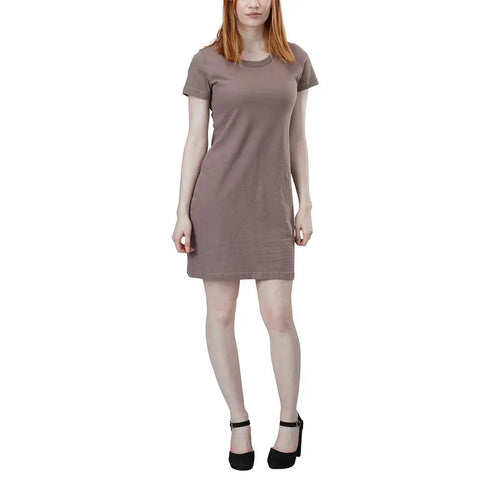 A person stands facing forward against a white background, wearing the Spiritex | Sustainable Apparel Short Sleeve Crewneck T-Shirt Dress in taupe with black ankle-strap heels.