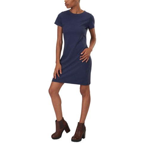 A person wears the Spiritex | Sustainable Apparel Short Sleeve Crewneck T-Shirt Dress in navy blue with brown ankle boots, standing against a white background.
