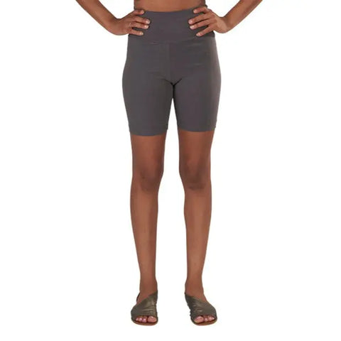 A person stands with hands on hips, wearing Spiritex | Sustainable Apparel Yoga Shorts in gray organic cotton, knee-length, and open-toed sandals, set against a plain white background.