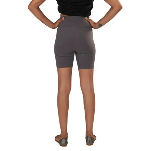 A person stands with hands on hips, wearing Spiritex | Sustainable Apparel Yoga Shorts in gray and a black top, viewed from the back against a white background.