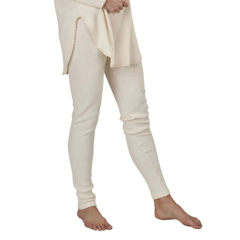 A person models Spiritex | Sustainable Apparel Thermal Leggings in off-white organic cotton with a matching top featuring side slits, standing barefoot against a white background. Only the lower half of their body is visible.