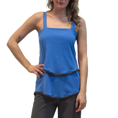 Model wears the Town Mountain Tiered Cami by Spiritex | Sustainable Apparel, a blue sleeveless top with grey trim, paired with dark pants and styled with one hand on her hip against a white background.