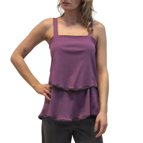 A woman poses with one hand on her hip, wearing the sleeveless purple Town Mountain Tiered Cami by Spiritex | Sustainable Apparel and dark pants.