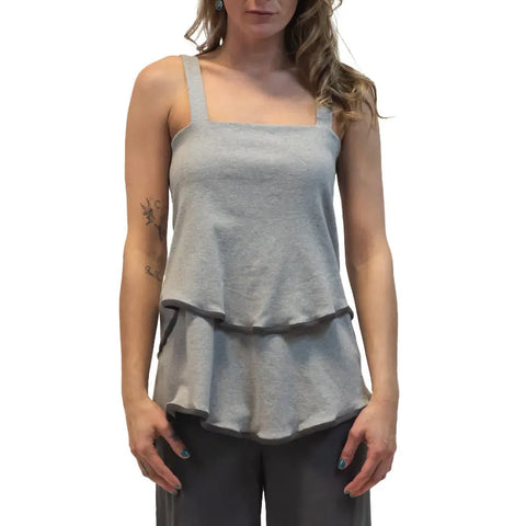 A woman models the Town Mountain Tiered Cami by Spiritex | Sustainable Apparel—a gray sleeveless top with wide straps and a ruffle hem, paired with matching pants. Made in the USA. She stands against a white background.