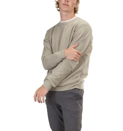 A person wears the Spiritex | Sustainable Apparel V-Inset Crewneck Sweatshirt in light beige over a white shirt and dark gray pants, standing against a white background with one arm bent, hand touching the opposite arm.