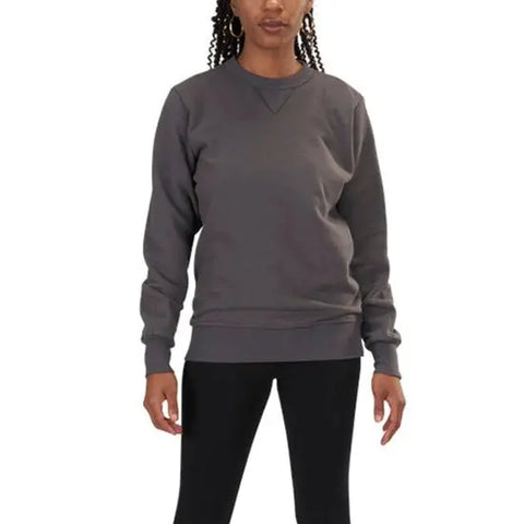 A woman with braided hair stands facing forward against a white background, wearing the Spiritex V-Inset Crewneck Sweatshirt in dark gray organic cotton and black pants, with her arms relaxed at her sides.