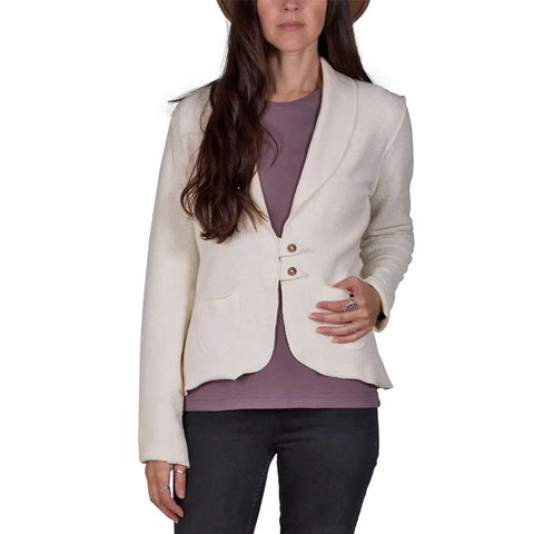 A woman with long dark hair and a hat wears the Spiritex Heavyweight Terry Tab Jacket in light beige over a mauve shirt and dark pants, standing against a white background.