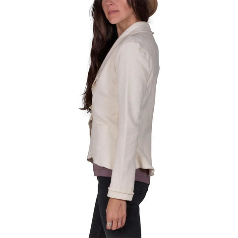 A woman with long dark hair, wearing the Spiritex Heavyweight Terry Tab Jacket over a mauve shirt and black pants, stands in profile against a white background. Her face is partially visible, and she wears a large ring on her finger.