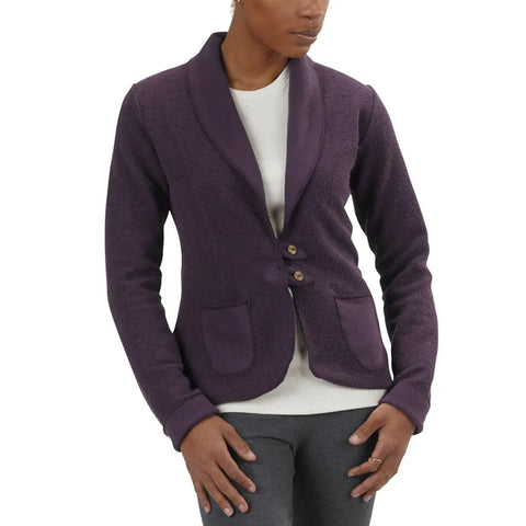 A person wearing a Spiritex | Sustainable Apparel Heavyweight Terry Tab Jacket in dark purple with a textured finish, shawl collar, two buttons, and front pockets over a white shirt and dark gray pants. The face is partially out of frame.