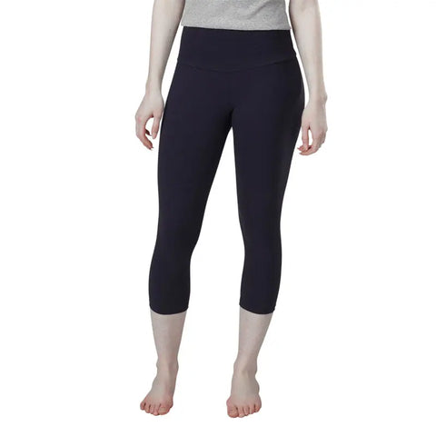 A person models the Spiritex | Sustainable Apparel Yoga Capri in black organic cotton with a grey top, standing barefoot against a white background. Their face is not shown.
