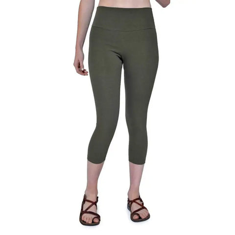 A person wearing Spiritex | Sustainable Apparel Yoga Capri in olive green stands on a white background, paired with brown strappy sandals. Only the lower half of their body is shown.