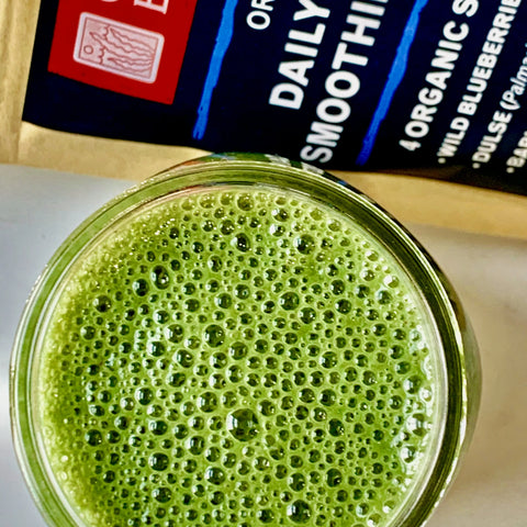 A glass of green smoothie with a bubbly surface sits next to an Oceans Balance Detox Smoothie Powder package, suggesting it contains organic detox blend packed with superfood powder ingredients.