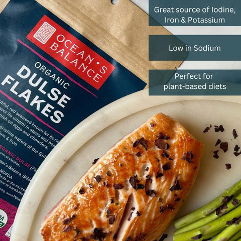 A plate with cooked salmon, asparagus, and USDA Organic seaweed flakes sits beside a pack of Ocean’s Balance Organic Dulse Flakes. Highlights: high in iodine, iron, potassium; low sodium; plant-based friendly.