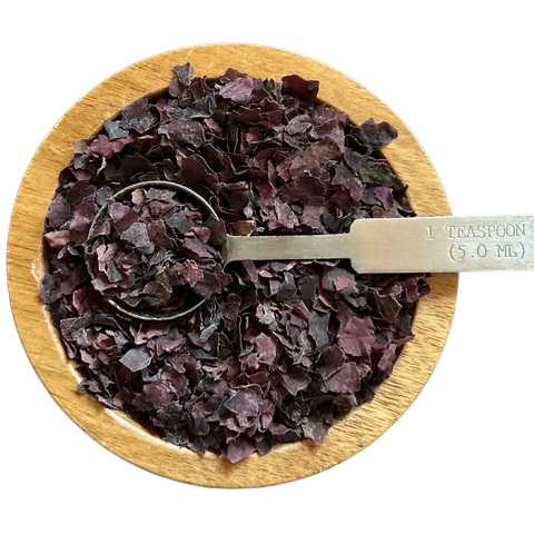 A wooden bowl contains Oceans Balance Organic Dulse Flakes, USDA Organic certified, with a metal teaspoon marked 1 TEASPOON (5.0 ML) partially buried in the seaweed flakes.