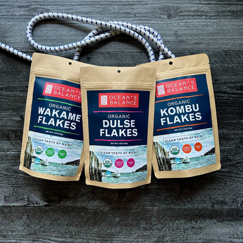 A brown resealable pouch of Ocean’s Balance Organic Dulse Flakes is displayed on a dark wooden surface with a white rope in the background.