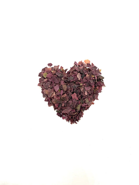 A heart made of dried purple and burgundy flower petals and Oceans Balance Organic Dulse Flakes is arranged on a plain white background.