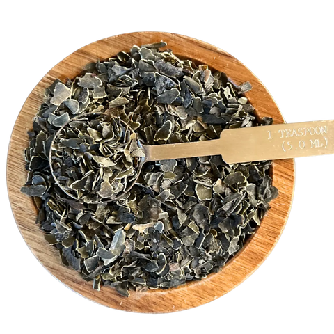 A wooden bowl holds Oceans Balance Organic Kombu Flakes, with a metal tablespoon (1 tsp/5.0 ml) scooping up some of the USDA Organic seaweed.