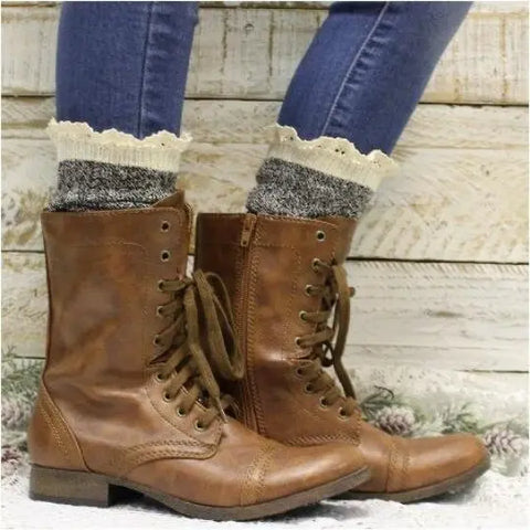 Catherine Cole ORGANIC Lace Boot Crew Socks in Salt N Pepper are styled under brown lace-up boots with zippers and blue skinny jeans, set against a rustic wooden wall and subtly patterned floor.