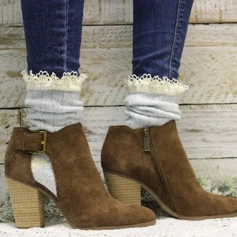 A person in blue jeans, Catherine Cole’s ORGANIC Lace Boot Socks in Carolina Blue, and brown suede ankle boots with chunky heels and side zippers stands against a rustic wooden background.