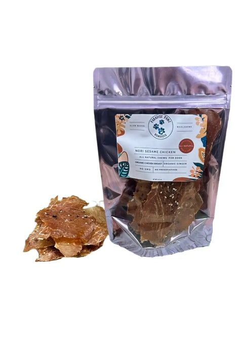 A silver resealable bag of Dogtown Bakery Nori Sesame Chicken stands upright with chicken jerky treats inside and a few scattered beside it, featuring Hawaiian-inspired organic dog treats on a white background.