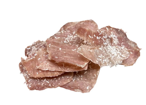 Dogtown Bakery’s Pork Luau features thin slices of jerky sprinkled with shredded coconut, artfully piled on a white background—a perfect tropical snack.