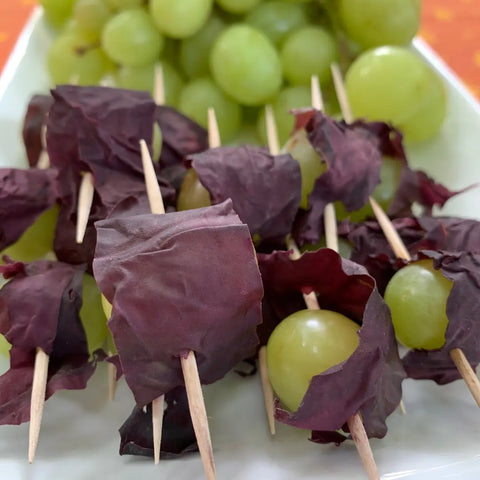 Green grapes skewered with toothpicks and wrapped in Oceans Balance Organic Whole Leaf Dulse, arranged on a white rectangular plate with extra green grapes in the background.