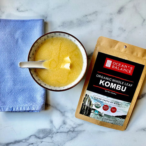 A bowl of miso soup with tofu and a spoon sits on marble beside a blue napkin and a pack of Oceans Balance Organic Whole Leaf Kombu.