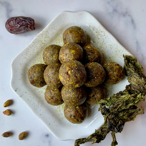 A plate featuring Oceans Balance Organic Whole Leaf Sea Lettuce with brownish-green energy balls, pistachios, and a date on white marble—invoking Gulf of Maine-inspired flavors.